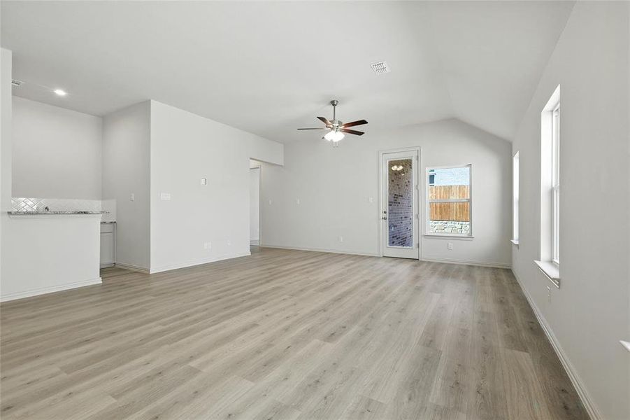 Unfurnished living room featuring ceiling fan, light wood-type flooring, and lofted ceiling Unfurnished living room featuring ceiling fan, light wood-type flooring, and lofted ceiling