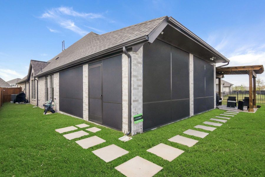 This photo features a modern brick home with a well-maintained lawn and paved walkway. The backyard includes a covered patio area, perfect for outdoor relaxation.