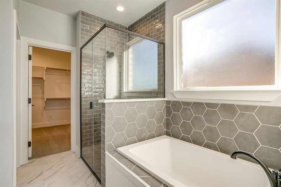 Bathroom featuring a bath, a spacious closet, light marble finish flooring, and a stall shower