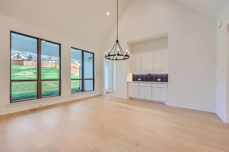 Unfurnished dining area with high vaulted ceiling, light hardwood / wood-style flooring, and an inviting chandelier