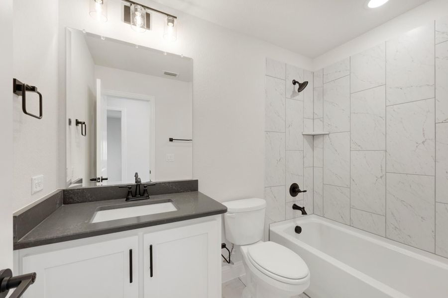 Bathroom with white vanity, dark countertop, tub-shower combo with marble-look tile, and black fixtures