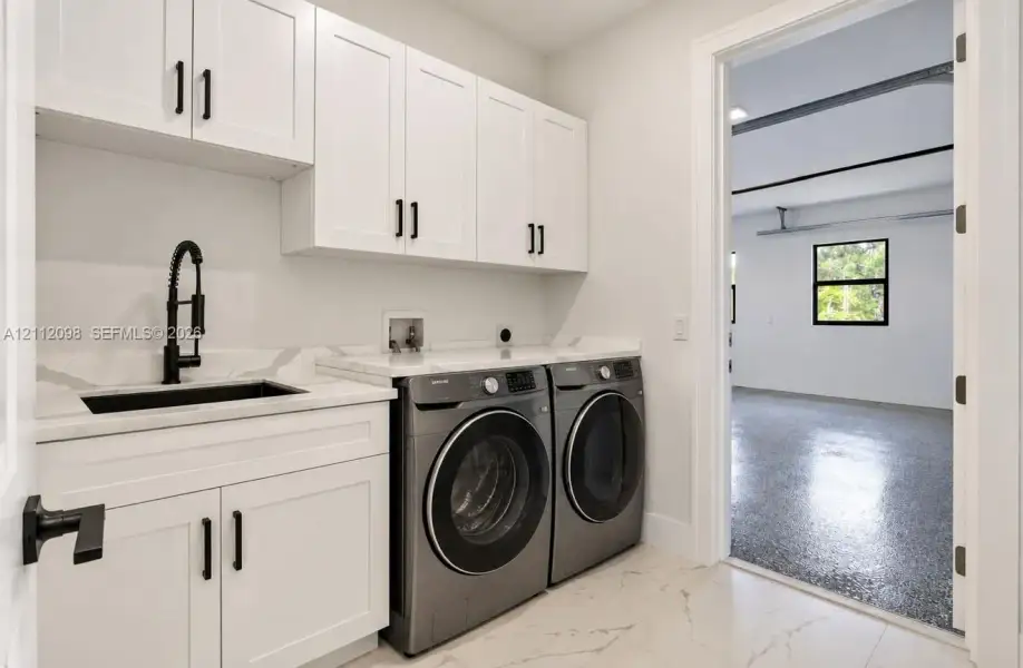 Utility space featuring white shaker-style cabinetry, stone-finish countertops, an undermount sink with a matte black pull-down faucet, and porcelain tile flooring Utility space featuring white shaker-style cabinetry, stone-finish countertops, an undermount sink with a matte black pull-down faucet, and porcelain tile flooring