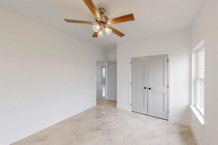 Unfurnished bedroom featuring ceiling fan, a closet, and light marble finish flooring
