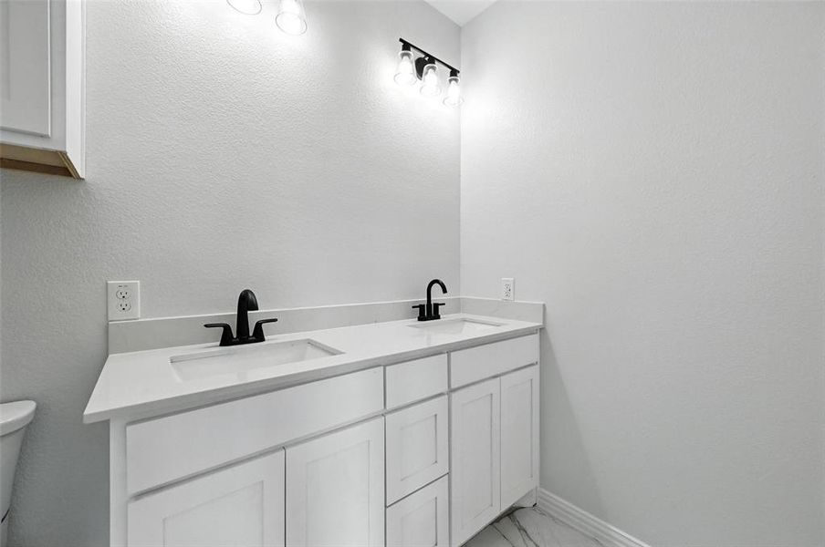 Bathroom with double vanity, a textured wall, and light marble finish flooring