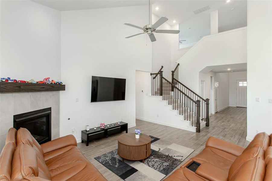 Two-story living area featuring a fireplace with a wood mantel, a ceiling fan, a staircase with dark wood newel posts and metal balusters, and wood-finish flooring