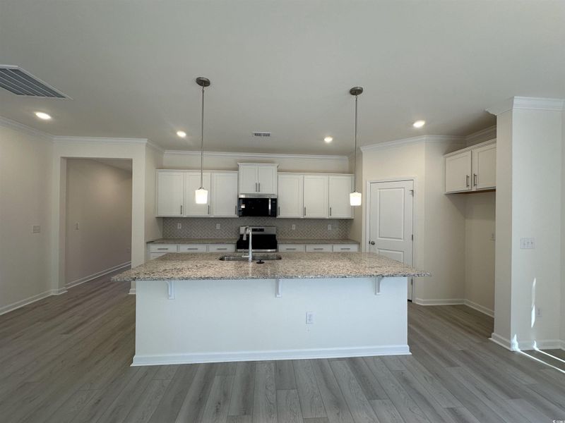 Kitchen with white cabinetry, a breakfast bar area, light stone countertops, a kitchen island with sink, and appliances with stainless steel finishes