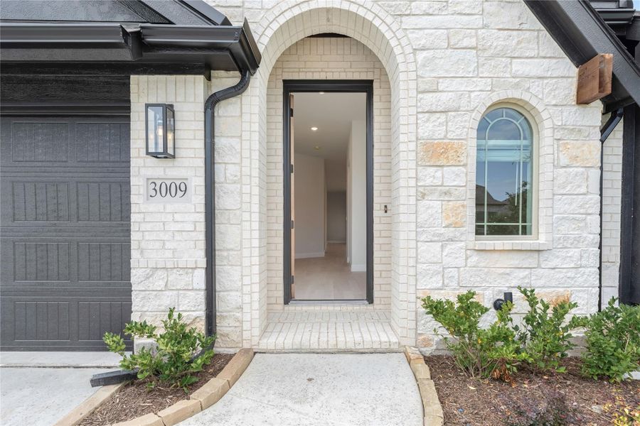 Home entrance with arched stone surround, dark front door, and attached garage with house number 3009