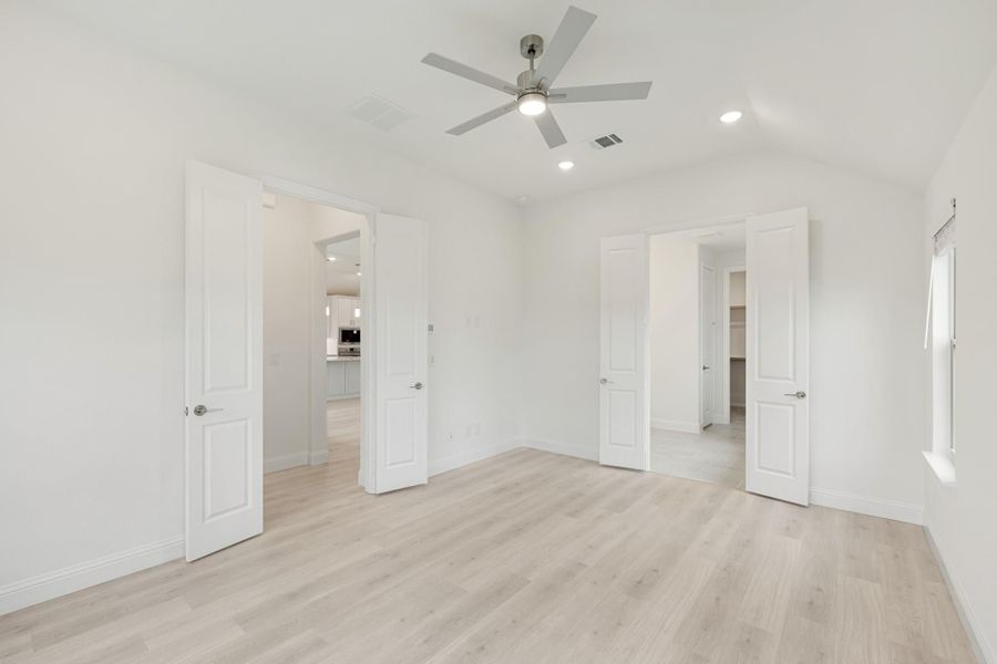 Empty bedroom with light wood floors, ceiling fan, and two open doorways leading to other rooms