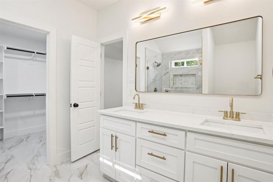 Bathroom featuring double vanity, light marble finish floors, a marble finish shower, and a spacious closet Bathroom featuring double vanity, light marble finish floors, a marble finish shower, and a spacious closet
