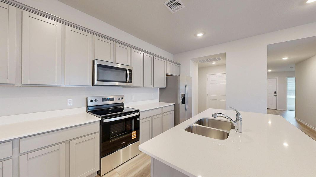Modern kitchen featuring light gray cabinetry, stainless steel appliances, white countertops, and a double basin sink on the island
