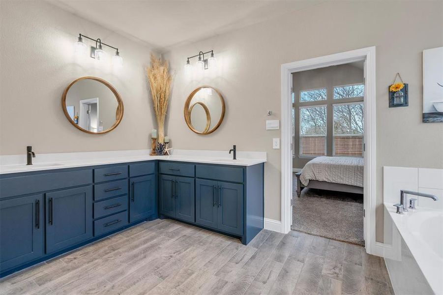 Ensuite bathroom with double vanity, light wood-type flooring, and a garden tub