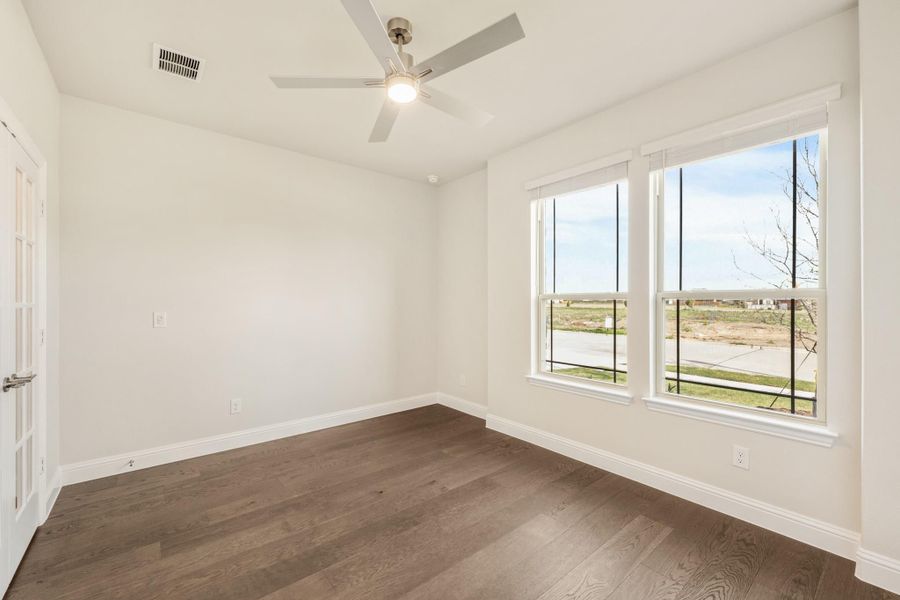 Empty bedroom with dark hardwood floors, ceiling fan, and large windows with outdoor views Empty bedroom with dark hardwood floors, ceiling fan, and large windows with outdoor views