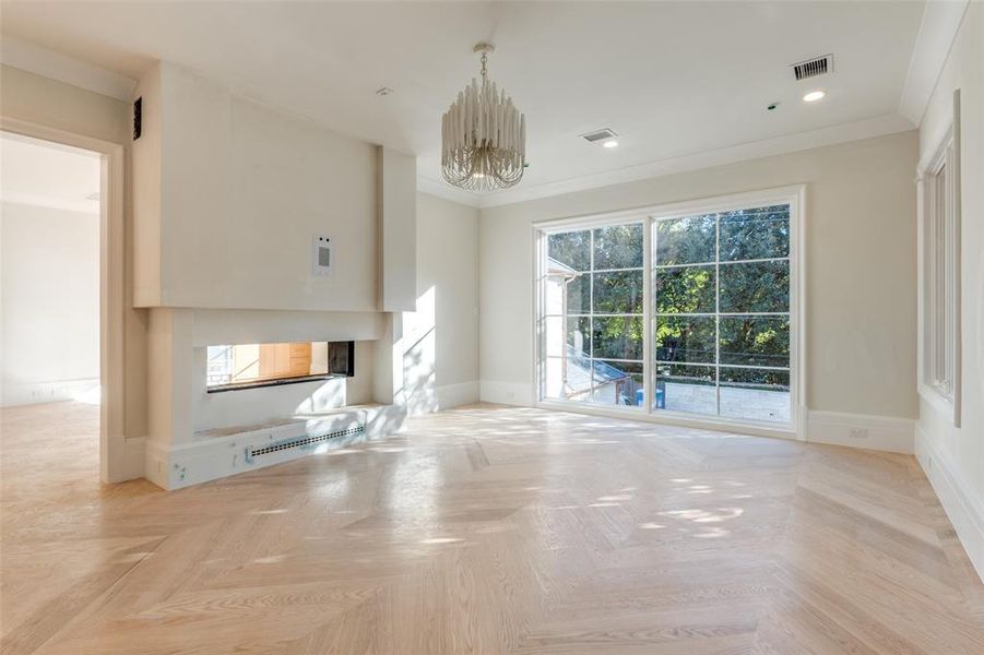 Unfurnished living room with an inviting chandelier, a multi sided fireplace, crown molding, and light parquet floors