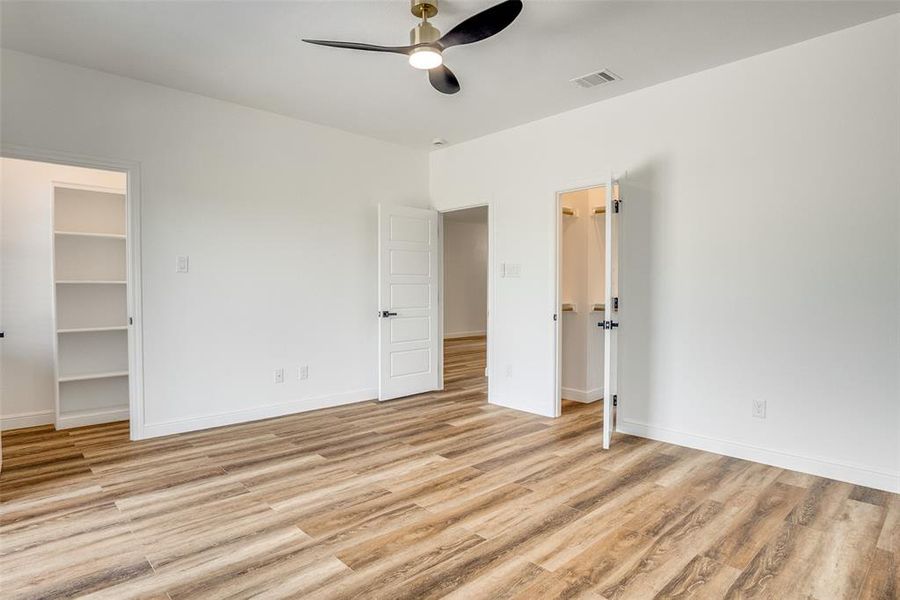 Unfurnished bedroom featuring a spacious closet, light wood-style flooring, and a ceiling fan