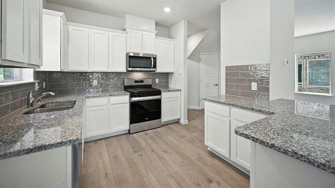 Kitchen featuring appliances with stainless steel finishes, white cabinets, dark stone countertops, light wood-style flooring, and recessed lighting