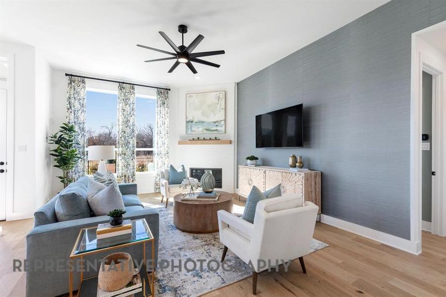 Living area featuring light wood-style flooring, a glass covered fireplace, a ceiling fan, and wallpapered walls
