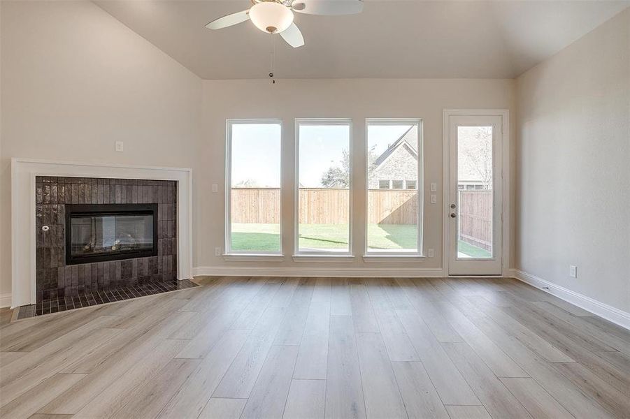 Unfurnished living room with a tile fireplace, ceiling fan, light hardwood / wood-style flooring, and vaulted ceiling