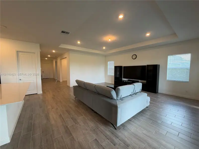 Open floor plan featuring a tray ceiling, recessed lighting, wood-finish flooring, and horizontal window blinds