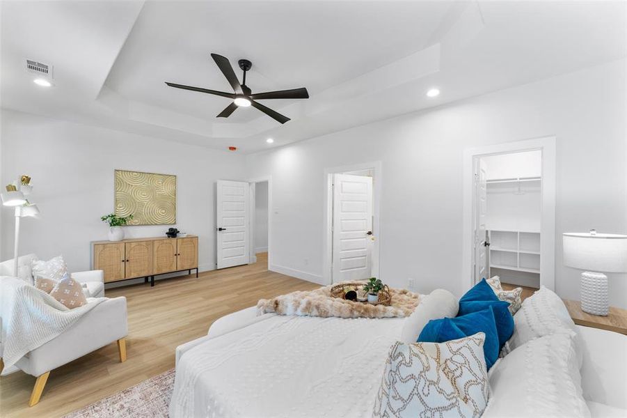 Bedroom with light wood-style flooring, a spacious closet, a raised ceiling, recessed lighting, and a ceiling fan