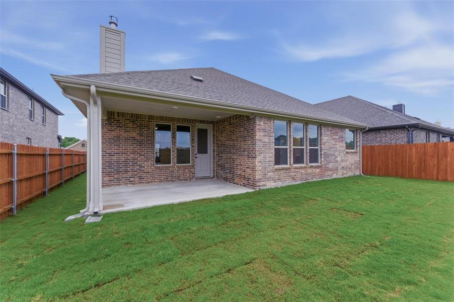 Expansive rear yard featuring a covered patio, brick exterior, multiple windows, and a privacy fence