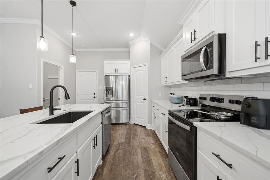 Kitchen with stainless steel appliances, light stone countertops, white cabinets, crown molding, and dark wood-style flooring