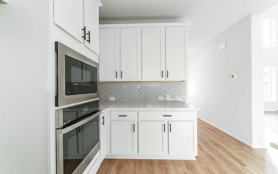 Kitchen with appliances with stainless steel finishes, white cabinetry, decorative backsplash, and light wood-style flooring