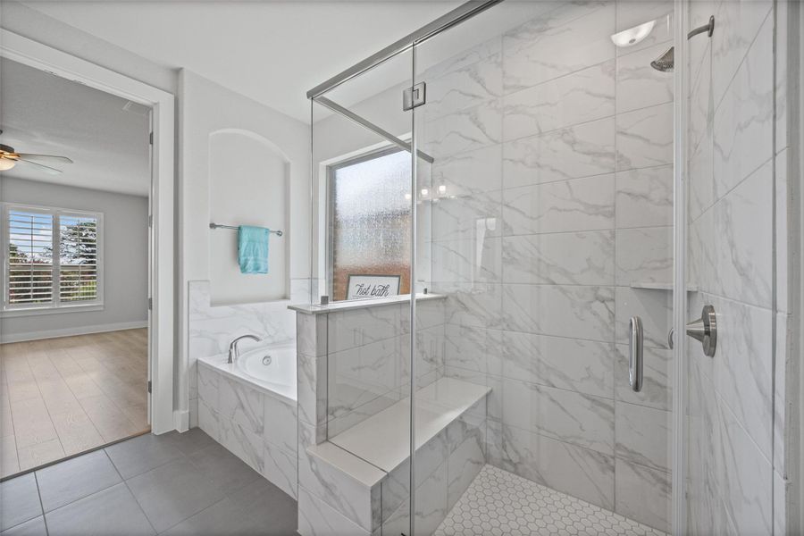 Luxurious bathroom features a spacious soaking tub and a walk-in shower with elegant marble-patterned tile.