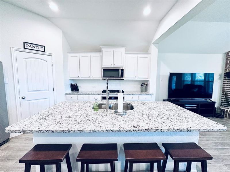 Kitchen with backsplash, vaulted ceiling, a kitchen island with sink, and light wood-type flooring