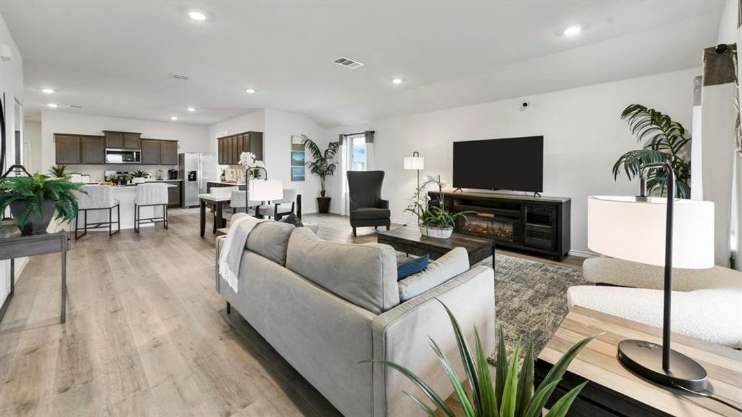 Open-concept living area featuring wood-finish flooring, recessed lighting, and a modern kitchen with dark cabinetry and stainless steel appliances Open-concept living area featuring wood-finish flooring, recessed lighting, and a modern kitchen with dark cabinetry and stainless steel appliances
