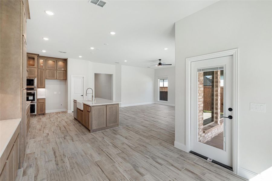 Open-concept kitchen and living area with center island, wood-look tile floors, and brown cabinets