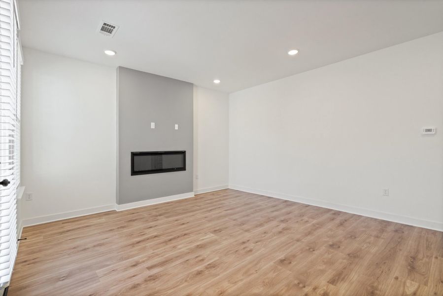 Spacious room featuring wood-finish flooring, recessed lighting, and a modern linear fireplace with a gray accent wall