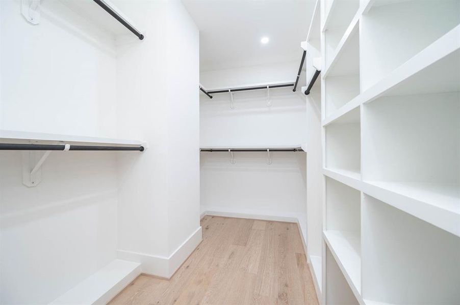 This is a spacious, well-organized walk-in closet featuring ample shelving and hanging space, with a clean, modern design and bright lighting.