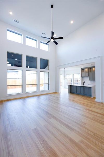 Unfurnished living room with light wood-style flooring, a high ceiling, recessed lighting, a ceiling fan, and a chandelier Unfurnished living room with light wood-style flooring, a high ceiling, recessed lighting, a ceiling fan, and a chandelier