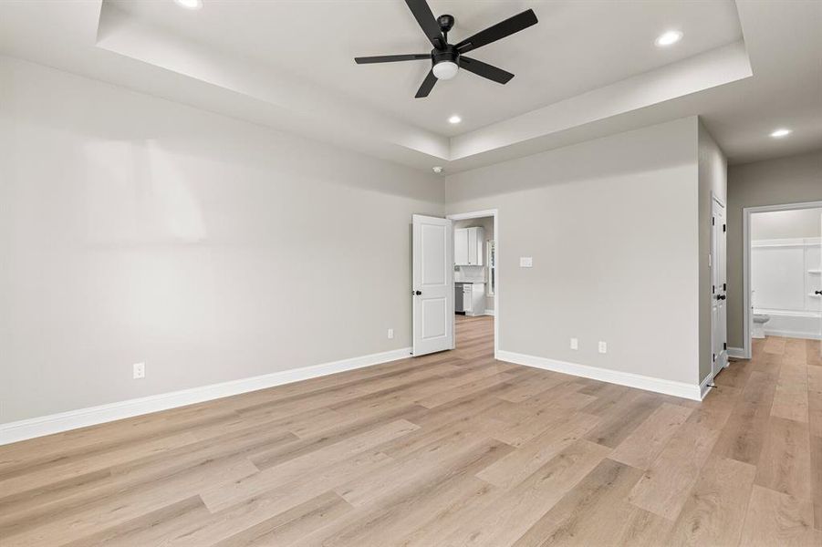 Unfurnished bedroom with a tray ceiling, ensuite bath, a ceiling fan, light wood-style flooring, and recessed lighting Unfurnished bedroom with a tray ceiling, ensuite bath, a ceiling fan, light wood-style flooring, and recessed lighting