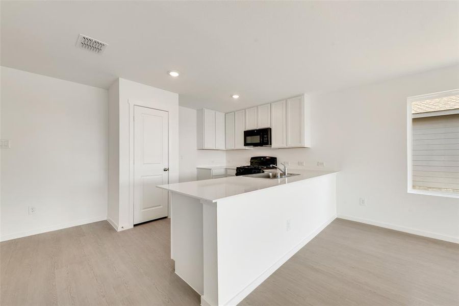 Kitchen with white cabinetry, a peninsula, light wood-style floors, black appliances, and recessed lighting Kitchen with white cabinetry, a peninsula, light wood-style floors, black appliances, and recessed lighting