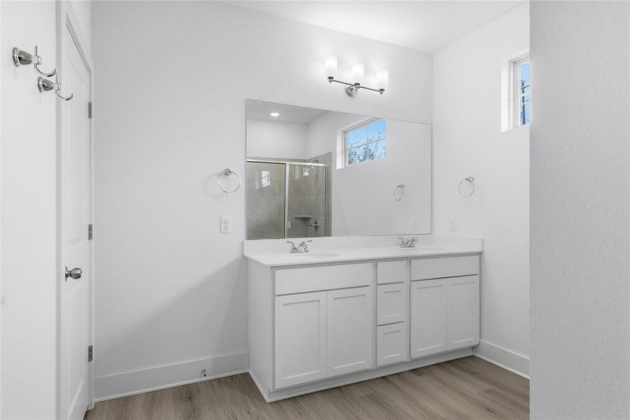 Full bath with double vanity, a stall shower, and light wood-style flooring