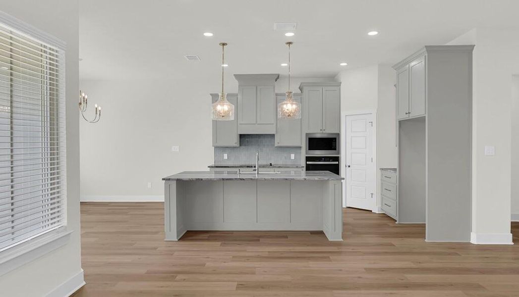 Kitchen featuring gray cabinetry, light stone countertops, backsplash, decorative light fixtures, and a center island with sink