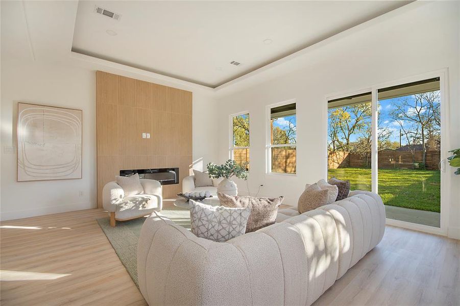 Living area featuring a tray ceiling, light wood-style flooring, and a tile fireplace Living area featuring a tray ceiling, light wood-style flooring, and a tile fireplace