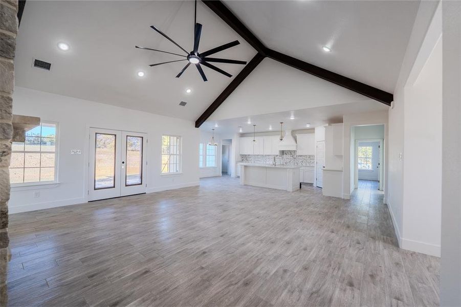 Unfurnished living room featuring beam ceiling, a ceiling fan, high vaulted ceiling, light wood-type flooring, and french doors Unfurnished living room featuring beam ceiling, a ceiling fan, high vaulted ceiling, light wood-type flooring, and french doors