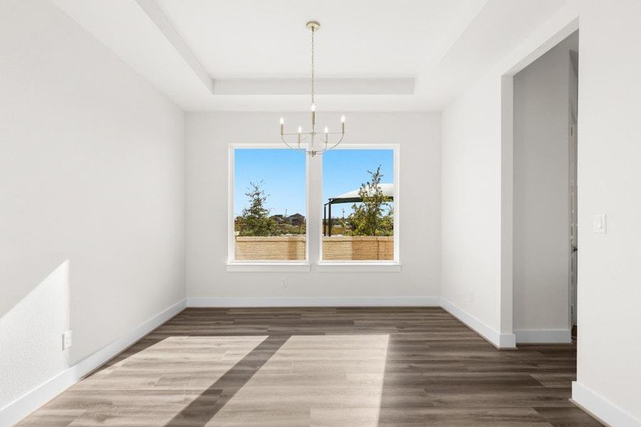 Unfurnished dining area featuring a chandelier, a tray ceiling, and dark wood finished floors Unfurnished dining area featuring a chandelier, a tray ceiling, and dark wood finished floors