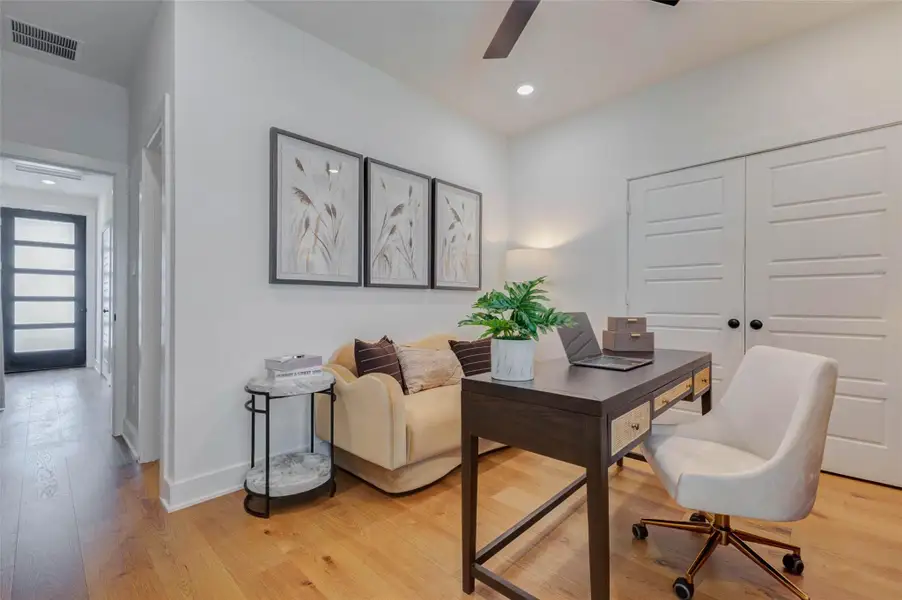 This flexible room offers an ideal setting for a home office, study, or creative space. Warm wood flooring, crisp white walls, recessed lighting, and a contemporary ceiling fan create a bright, comfortable environment. Double-door storage adds practical organization, while the nearby hallway and modern entry door contribute to the home’s cohesive, polished design.