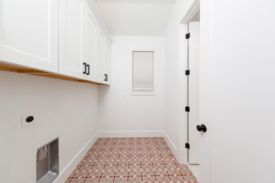 This bright and functional laundry room is conveniently located right off the primary walk-in closet and is ready for your appliances. It features clean white walls, trim, cabinets, window, and gorgeous tile flooring.