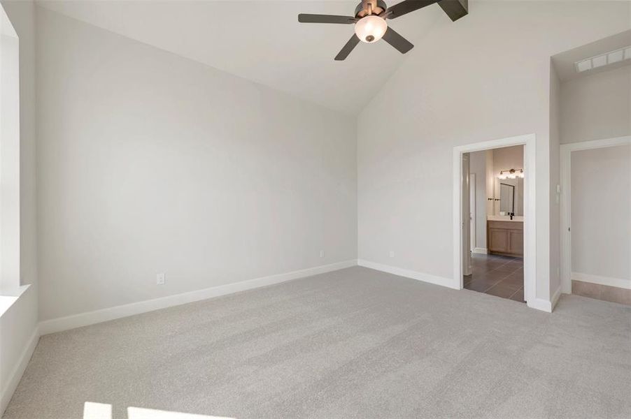 Spacious bedroom featuring vaulted ceilings, light gray carpeting, and a ceiling fan with integrated lighting