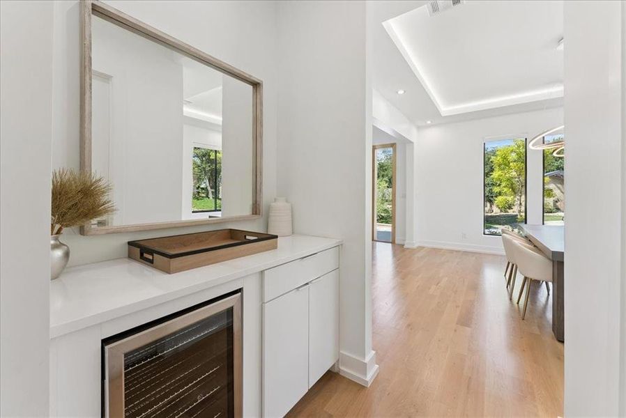 Bar area featuring beverage cooler, white cabinets, light wood-type flooring, recessed lighting, and light stone counters
