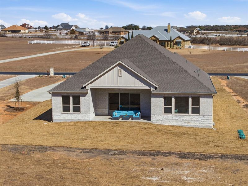 Rear view of property featuring a shingled roof, stone siding, board and batten siding, a residential view, and covered porch