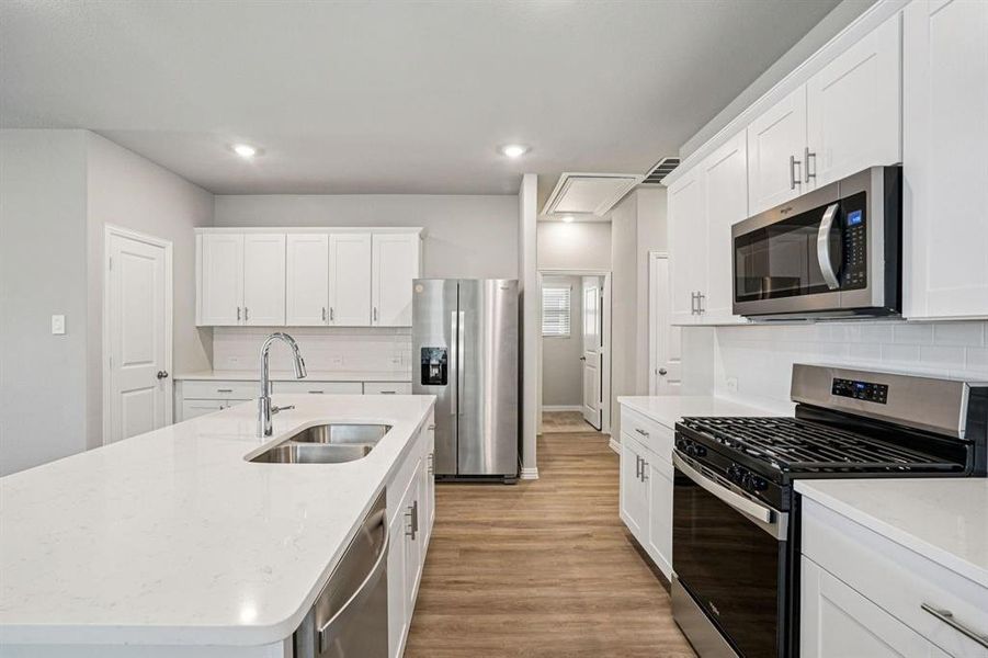 Kitchen featuring stainless steel appliances, white cabinets, light stone countertops, light wood finished floors, and recessed lighting