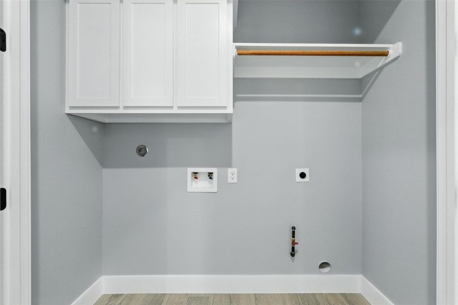 This laundry area features light gray walls, white cabinetry for storage, and hook-ups for a washer and dryer. There's a wooden rod for hanging clothes and the flooring is a light wood style, creating a clean and functional space.