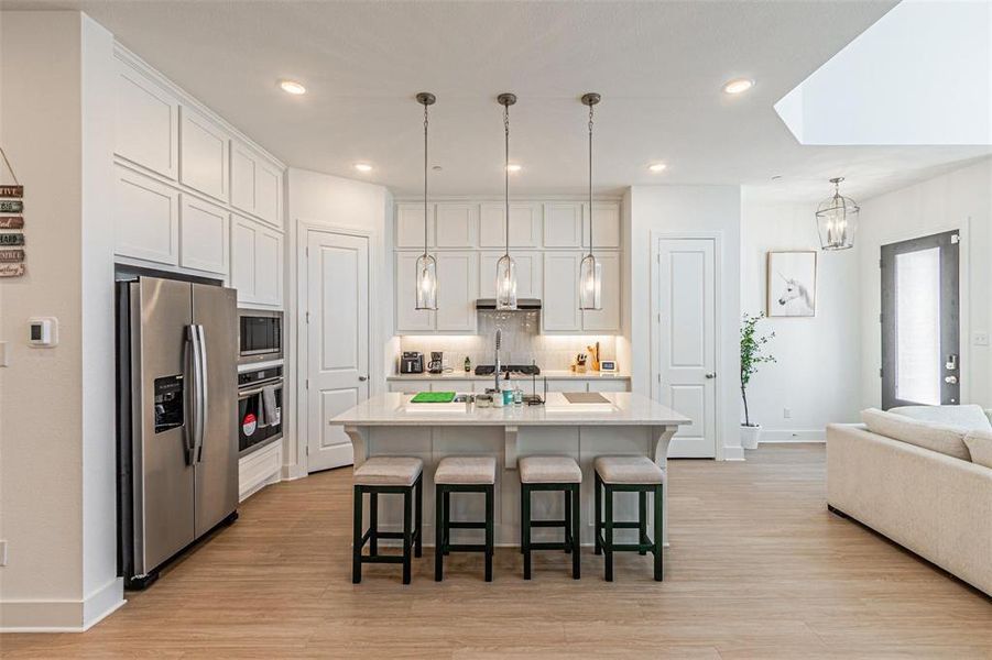 Kitchen featuring appliances with stainless steel finishes, tasteful backsplash, a breakfast bar area, a center island with sink, and hanging light fixtures