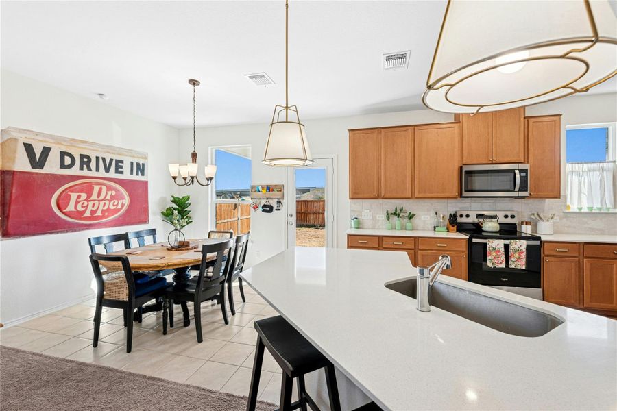 The kitchen showcases warm wood-finish cabinetry, an electric range and cooktop, stylish hanging pendant lighting, a stainless steel microwave, and a welcoming breakfast bar—perfect for everyday living and effortless entertaining.