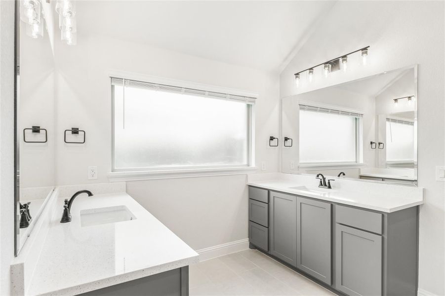 Bathroom with dual vanities, gray cabinets, white quartz countertops, and large mirrors with overhead lighting Bathroom with dual vanities, gray cabinets, white quartz countertops, and large mirrors with overhead lighting